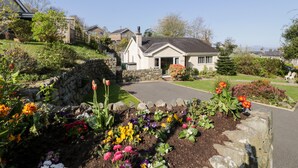 A residential house with a stone wall, a garden with colorful flowers, and a clear blue sky. - Clyd Fan (Harlech)