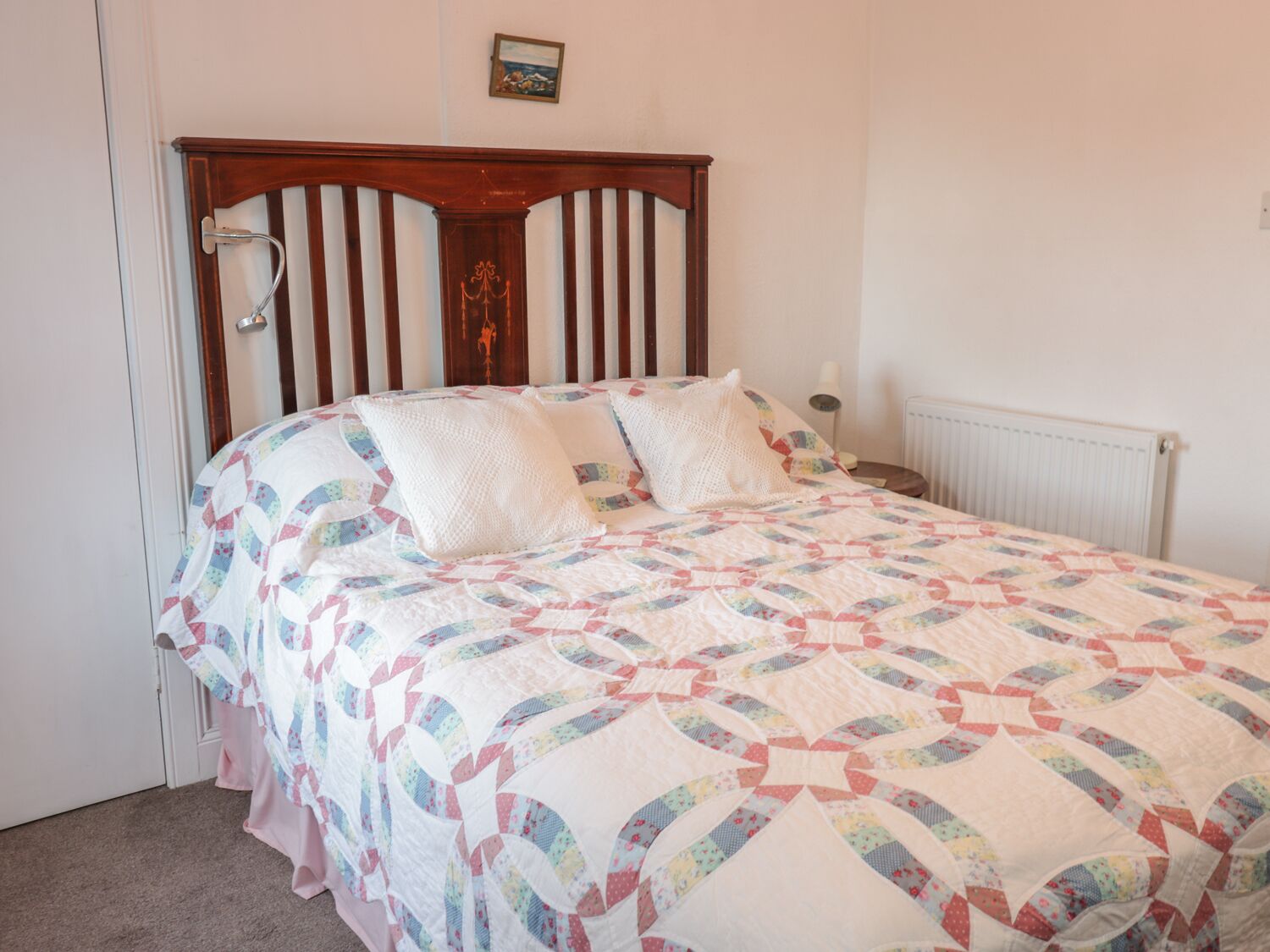 A single bed with a wooden headboard, a quilt with a geometric pattern, and a bedside table with a lamp.