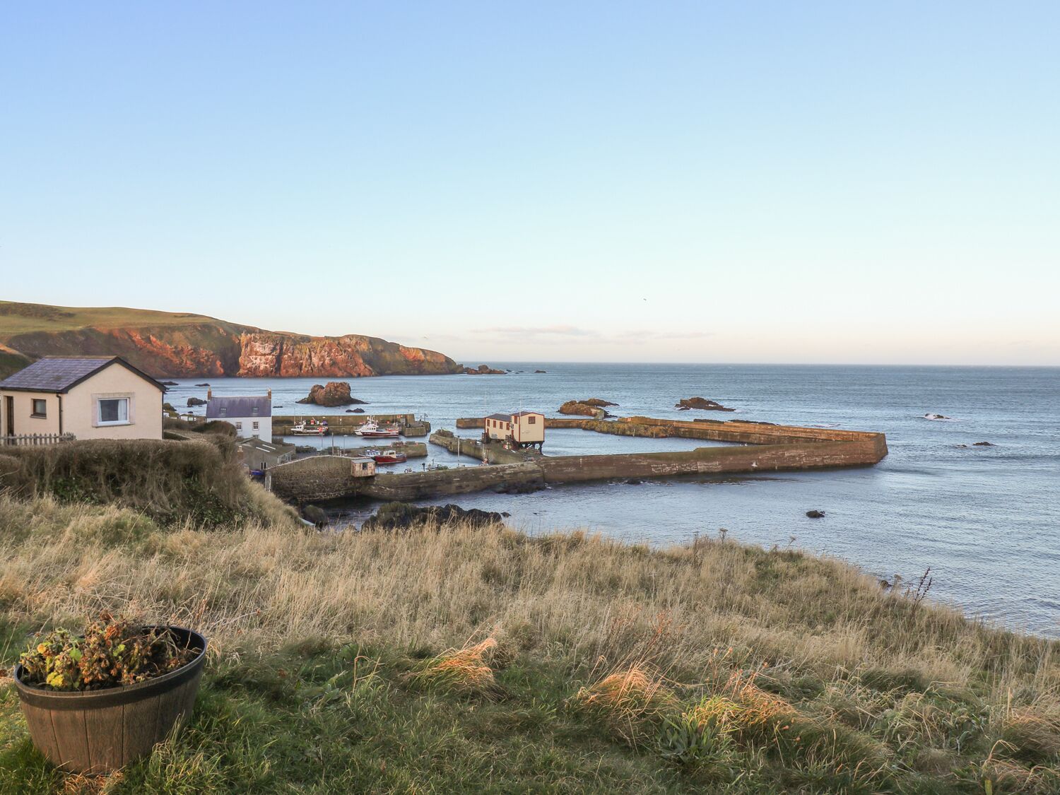 A coastal scene with a house, rocky breakwaters, and a calm sea.