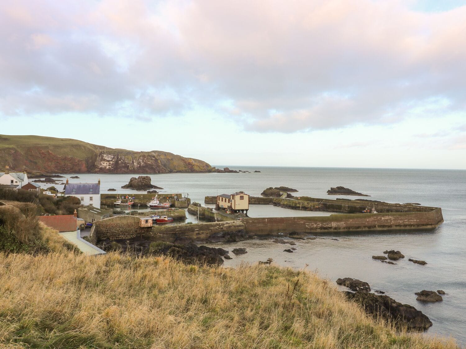 A coastal town with a prominent sea wall, a small harbor with boats, and buildings along the shore.