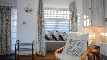 A cozy room with a bed, a chair, a wooden cabinet, and a window with curtains.