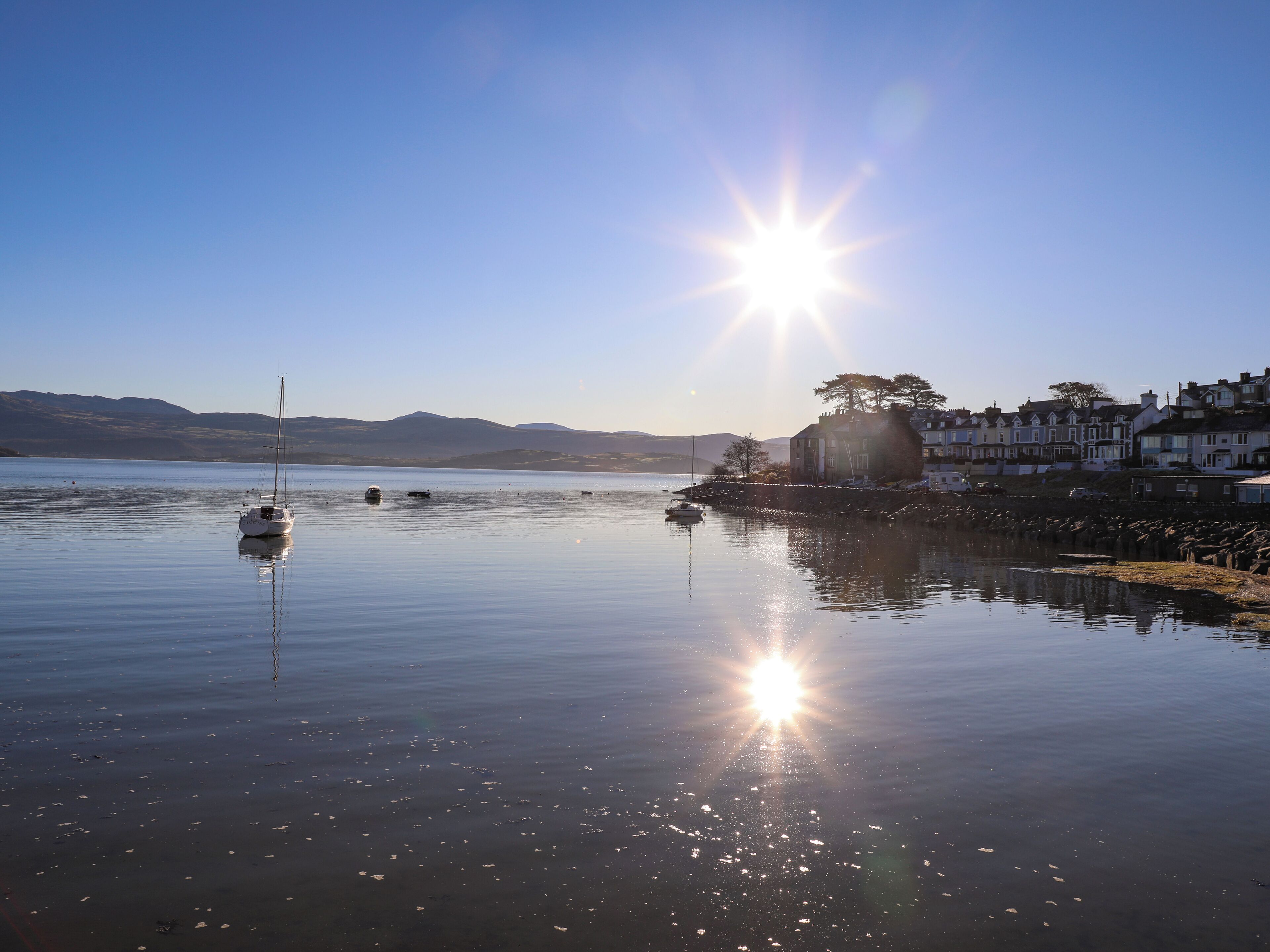 A calm lake with boats, a clear sky, and a row of houses along the shore.