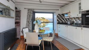 A kitchen with a view of a lake, a dining table with chairs, and a refrigerator. - St Agnes (Porthmadog)