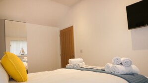 Habitación de hotel con cama, almohada amarilla, toallas enrolladas, televisión en la pared y puerta de madera.