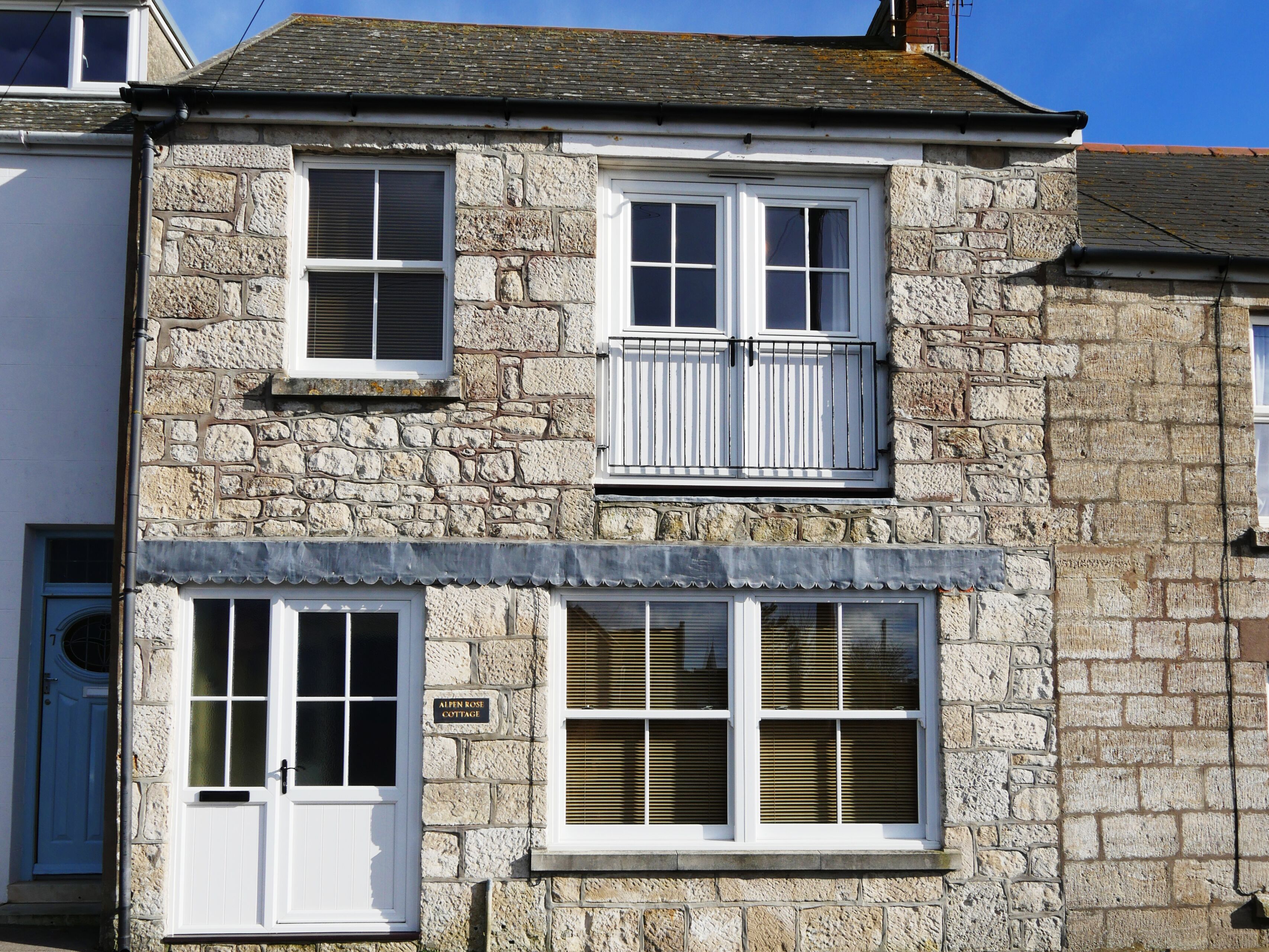 Un bâtiment en pierre avec deux fenêtres, une porte et une enseigne sur laquelle on peut lire : « Alpine Rose Cottage ».