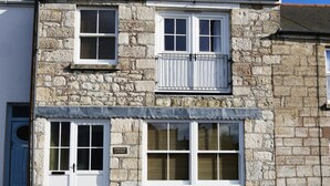 A stone building with two windows, a door, and a sign that reads "Alpine Rose Cottage."