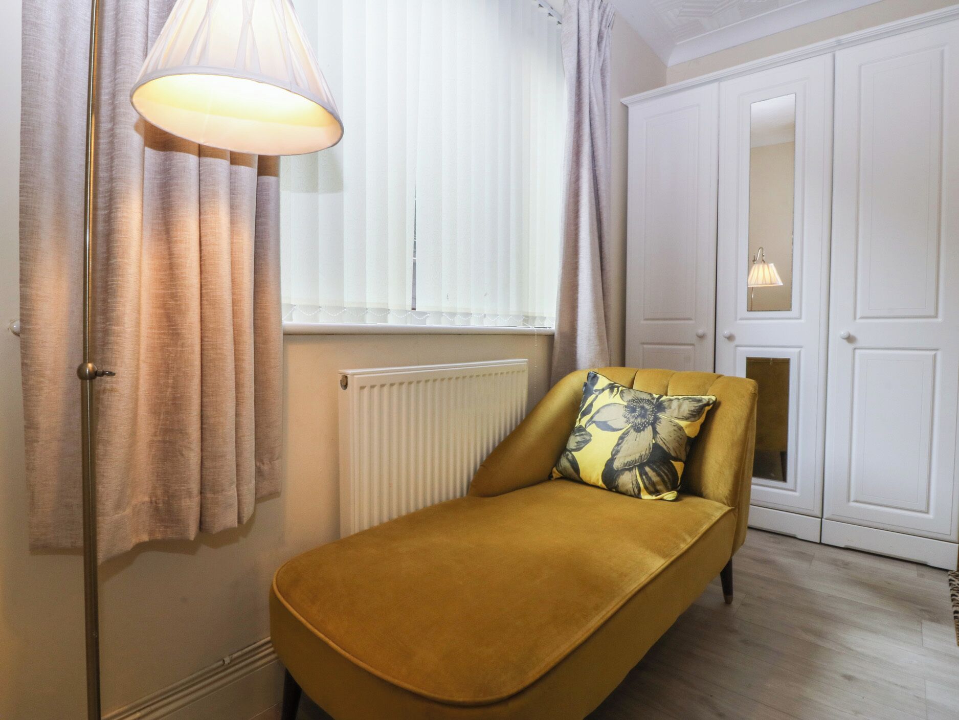 A room with a single sofa, a radiator, a window with blinds, a door, and a hanging light fixture.