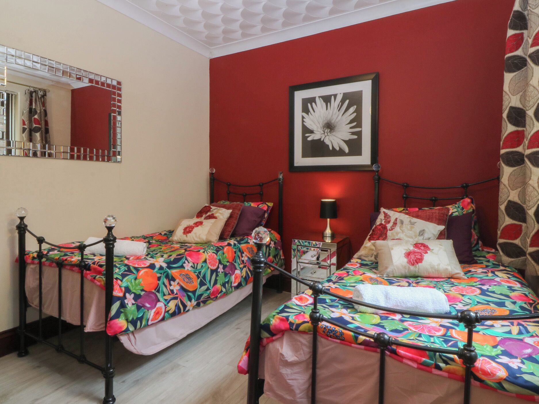 A bedroom with two single beds, a nightstand with a lamp, a framed picture on the wall, and a mirror above the bed.