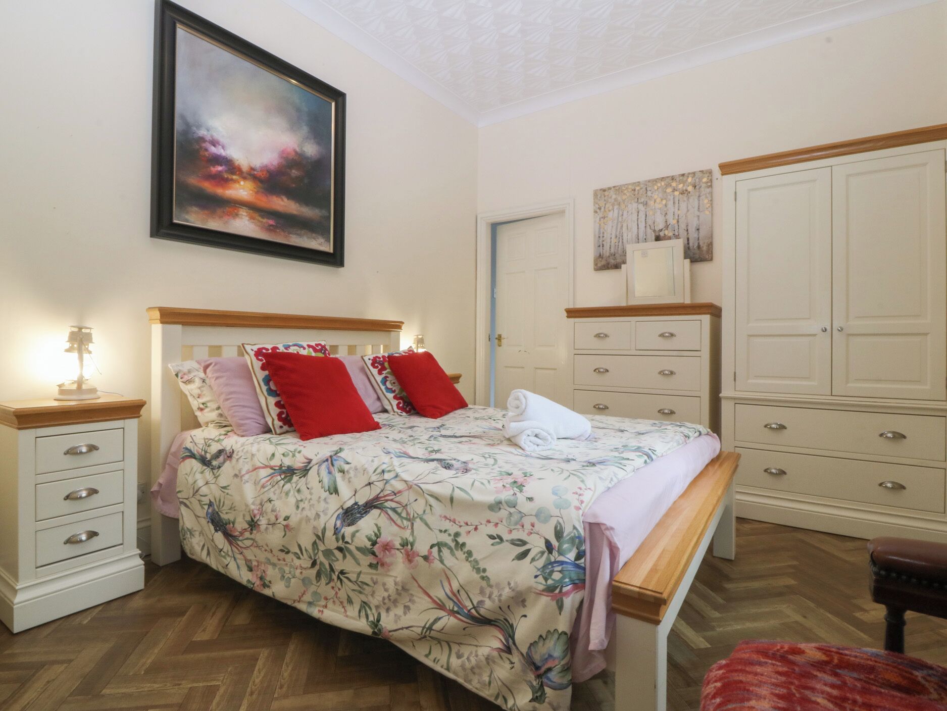 A bedroom with a bed, bedside tables, a dresser, a wardrobe, and a painting on the wall.