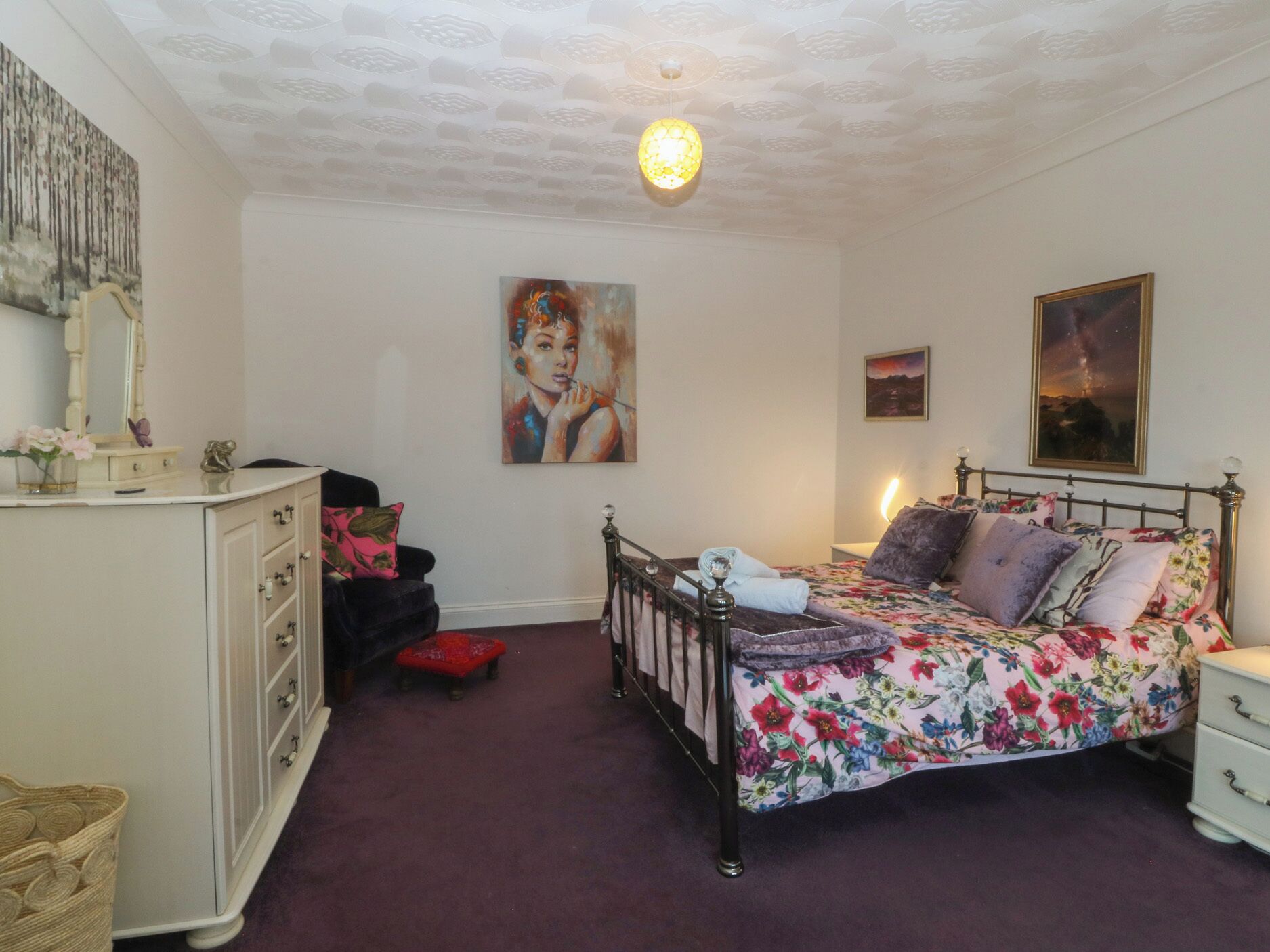 A bedroom with a bed, dresser, and artwork on the walls.