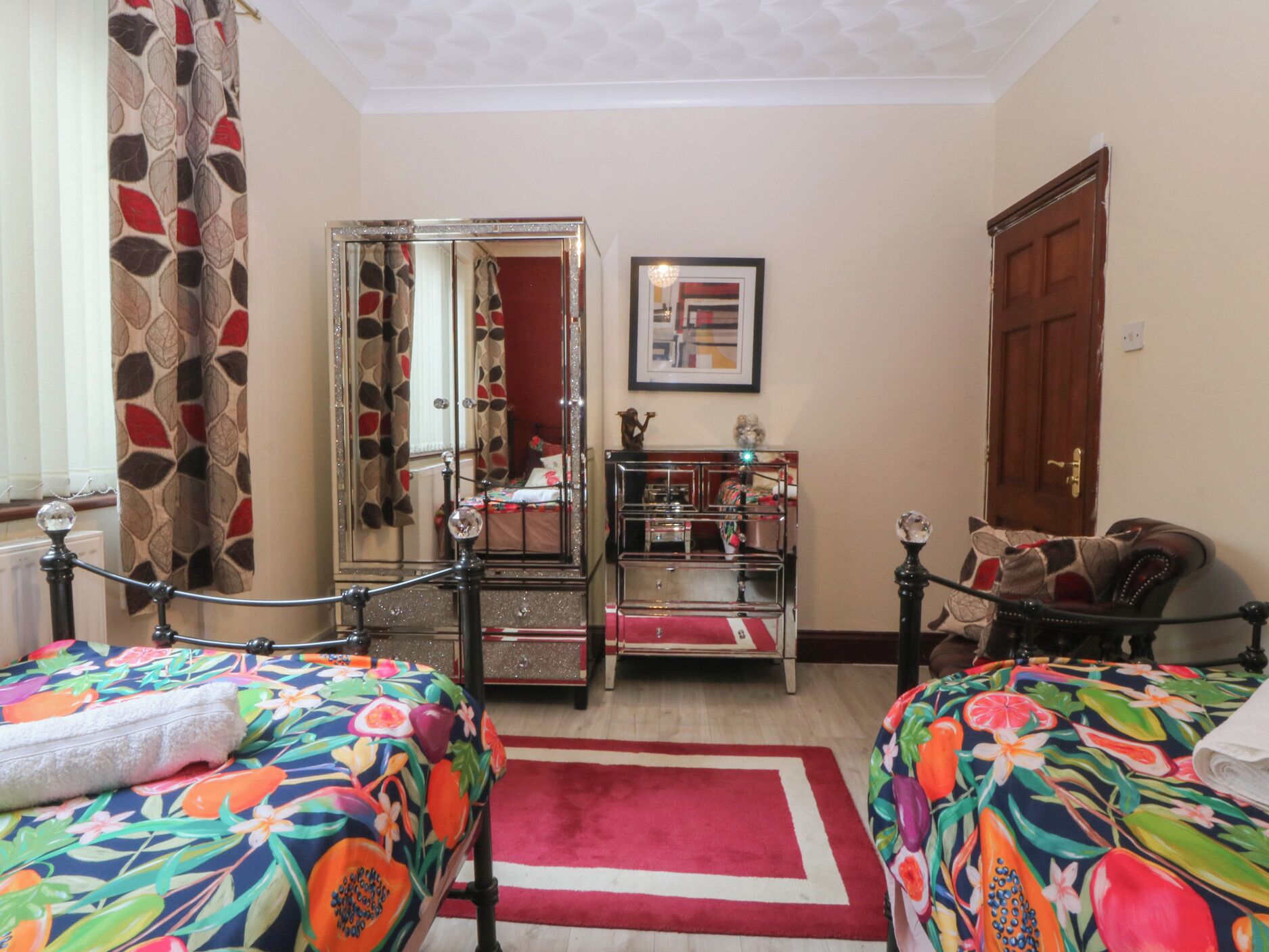 A bedroom with two beds, a dresser, a mirror, and a door.