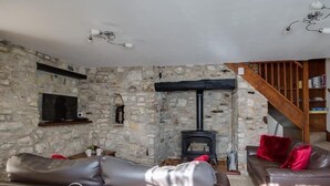A cozy living room with stone walls, a fireplace, leather sofas, and a staircase. - Blueberry Cottage (Weymouth)