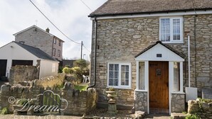 A stone cottage with a wooden door, white-framed windows, and a stone wall with a gate. - Blueberry Cottage (Weymouth)