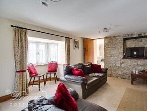 A cozy living room with a stone wall, a leather sofa, a wooden chair, and a television mounted on the wall.