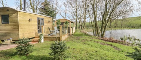 A wooden cabin with a deck, a small garden, and a view of a lake.