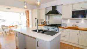 A modern kitchen with white cabinetry, a central island with a sink, a stainless steel stove, and pendant lighting. - Shady Bowers (Carnforth)