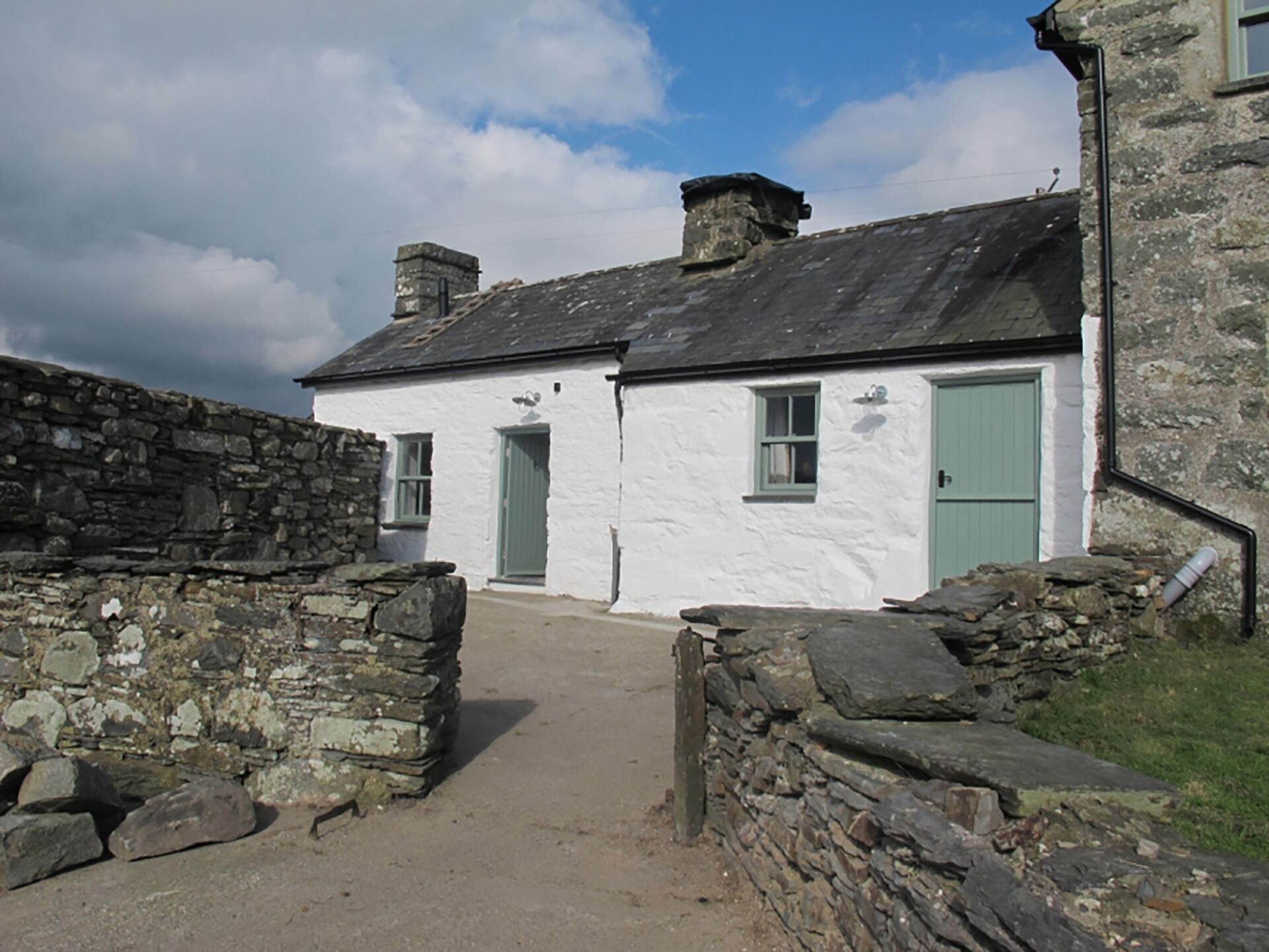 A white building with green doors and windows, a stone wall, and a stone staircase.