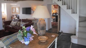 Ett vardagsrum med en brun lädersoffa, ett träbord med en vas med blommor, en lampa och en trappa som leder till ett annat rum.