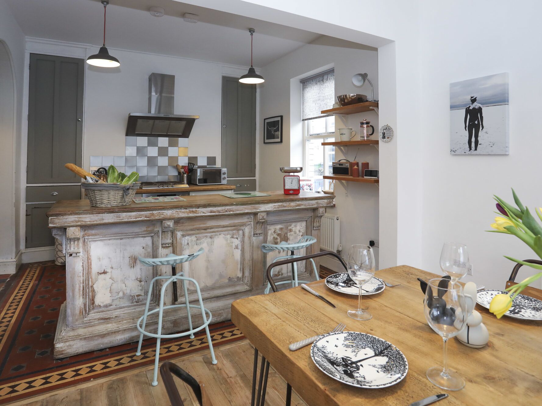 A kitchen with a central island, bar stools, a dining table set for two, and a view of the sea through a window.
