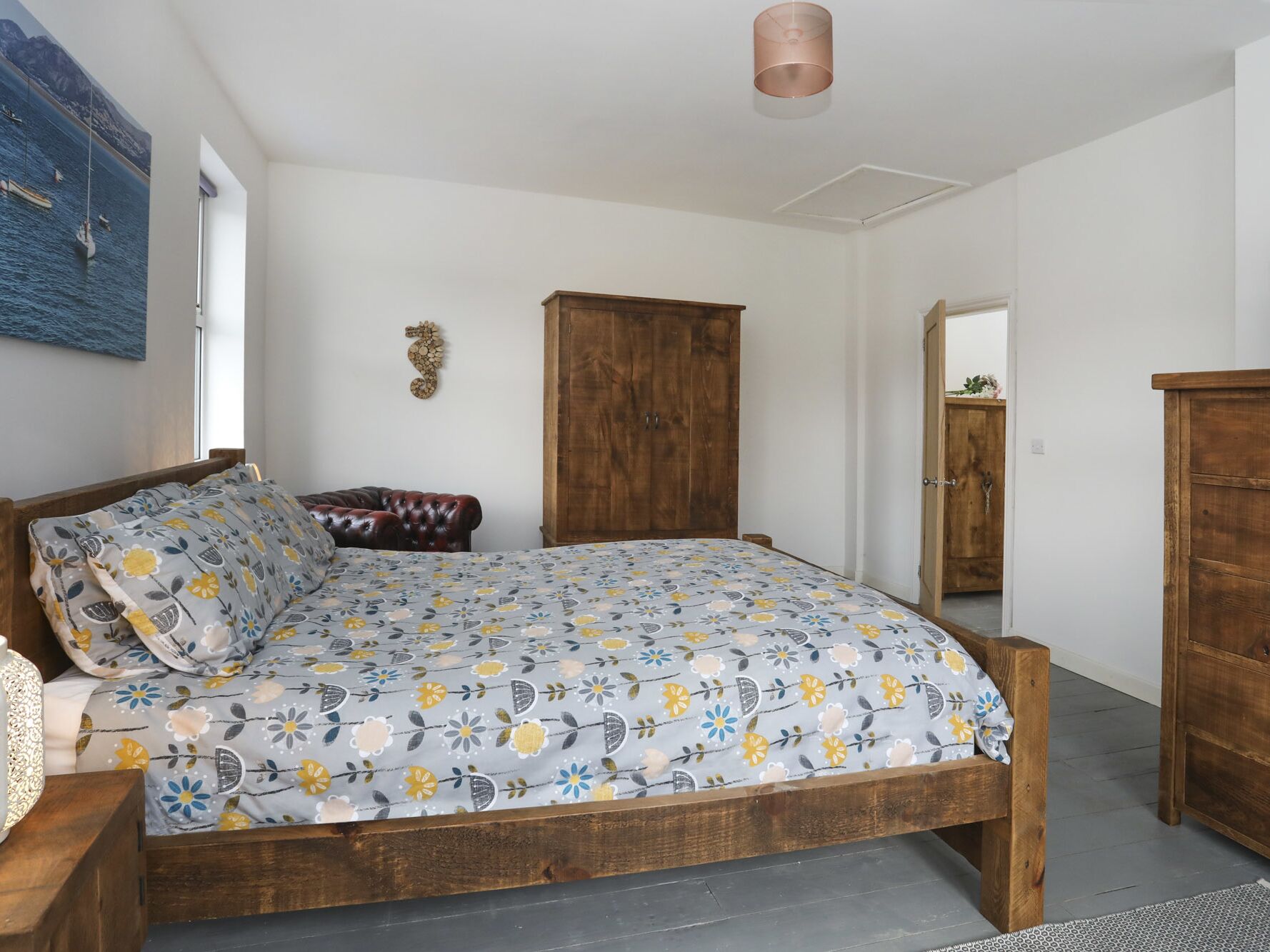 Een slaapkamer met een bed, een houten garderobe, een leren fauteuil en een kunstwerk aan de muur.