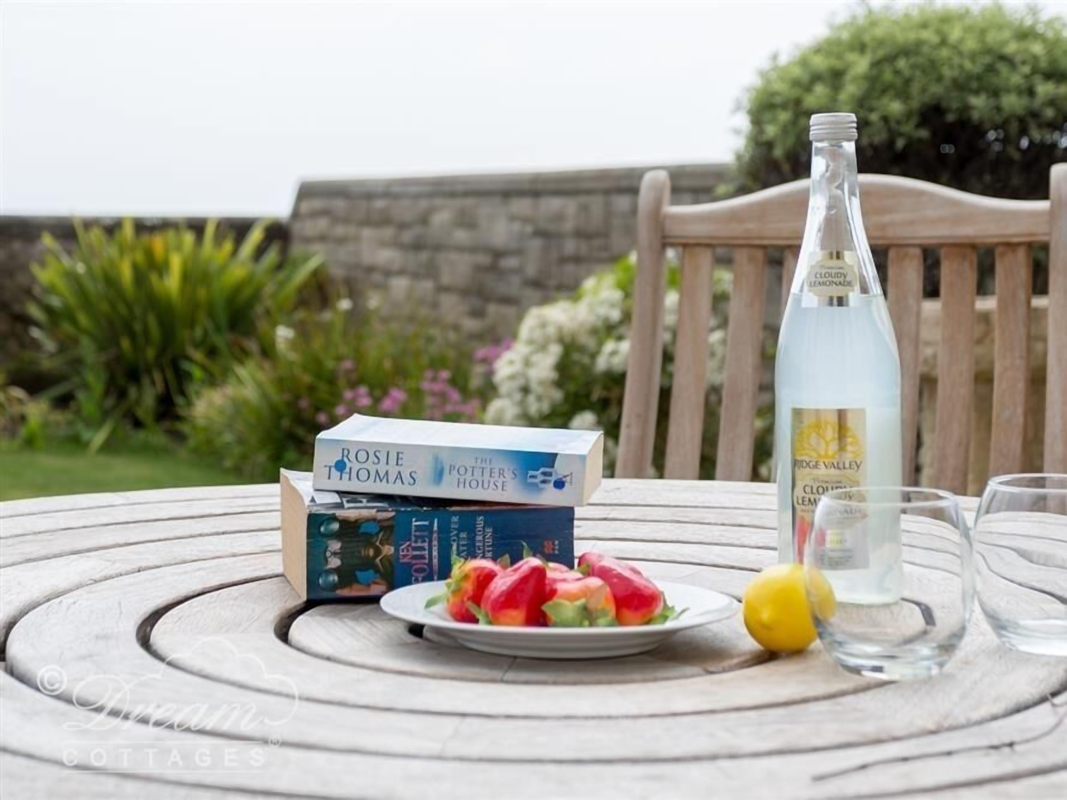 Una mesa con una pila de libros, una botella de Limonada Nublada, un plato de fruta y vasos.
