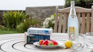 Una mesa con una pila de libros, una botella de Limonada Nublada, un plato de fruta y vasos.