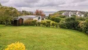A coastal property with a grassy lawn, a small shed, and a view of the sea. - Brambles (St Austell)