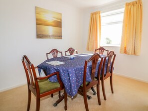 A dining room with a table set for six, surrounded by wooden chairs with green cushions. - Brambles (St Austell)