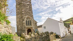 A stone tower with a pointed arch window, adjacent to a white building with a sign reading "JUST". - Brambles (St Austell)