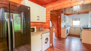 A log cabin with a kitchen featuring a refrigerator, microwave, toaster, and washing machine.