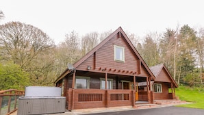 A wooden cabin with a porch, a hot tub, and a fenced yard.