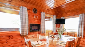 A wooden cabin interior with a dining table set for four, a fireplace, and a television mounted on the wall.