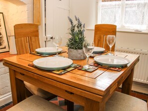 A wooden dining table with two chairs, two plates, two wine glasses, and a potted plant.