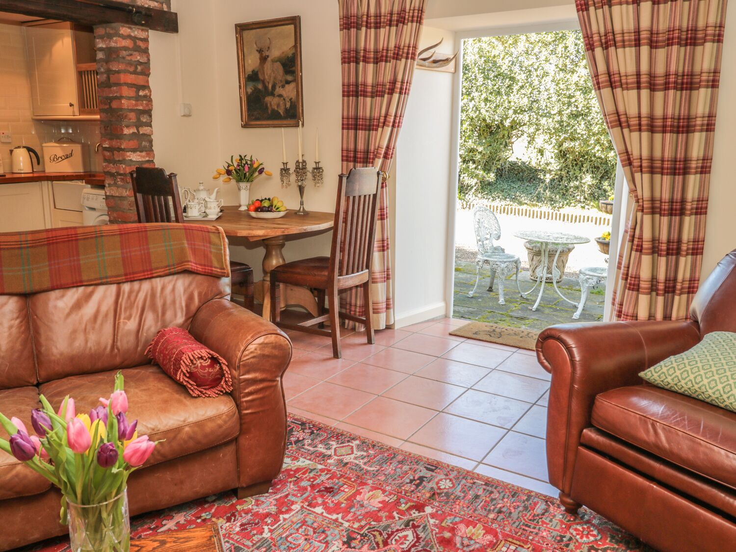 Un salon chaleureux avec un canapé en cuir marron, un tapis à motifs et un coin repas comprenant une table et des chaises.