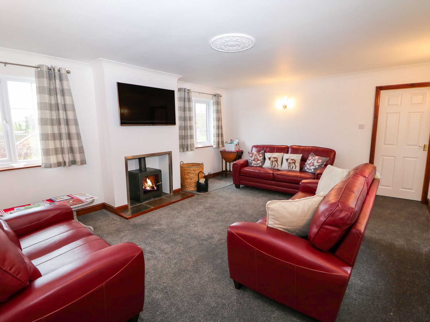 A living room with a fireplace, red leather sofas, a flat-screen TV, and a door.