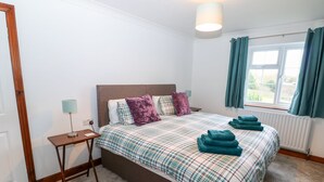 Une chambre à coucher avec un lit, une table de chevet, une lampe, une fenêtre avec des rideaux et un radiateur.