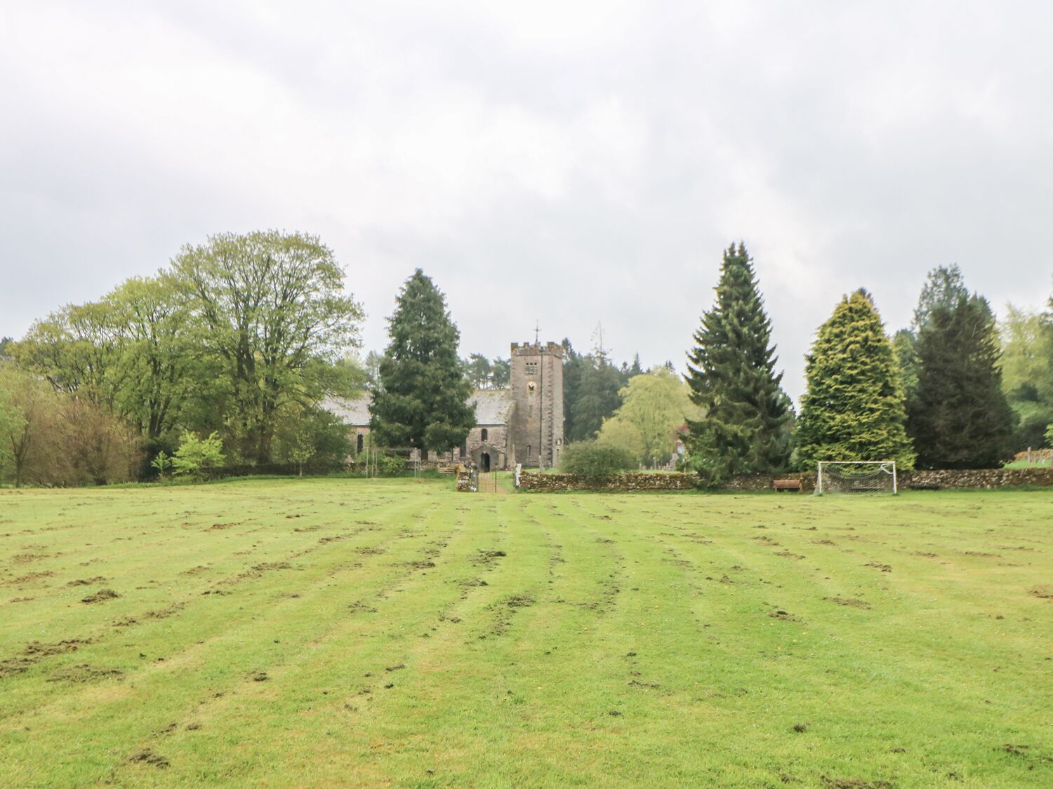 A grassy field with a stone building in the distance, surrounded by trees.