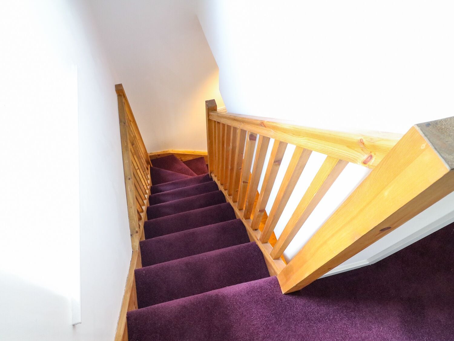 A wooden staircase with purple carpeted steps and a wooden handrail.