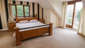 A bedroom with a large bed, wooden headboard, and a view of greenery through the window. - Shatterford Lakes (Bewdley)