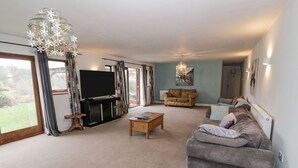 A spacious living room with a large TV, a wooden coffee table, a patterned sofa, and a chandelier. - Shatterford Lakes (Bewdley)