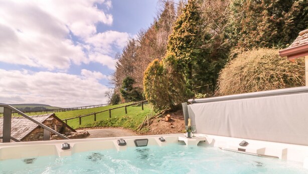 A hot tub with a clear view of the surrounding landscape, including a wooden structure and a grassy hill.