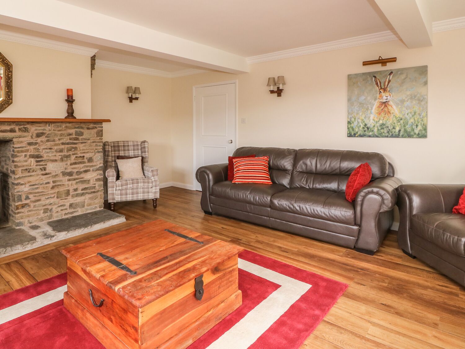 A living room with a stone fireplace, a leather sofa, a plaid armchair, and a wooden chest of drawers.