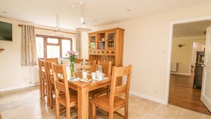A dining area with a wooden table and chairs, a cabinet with glass doors, and a television on the wall.
