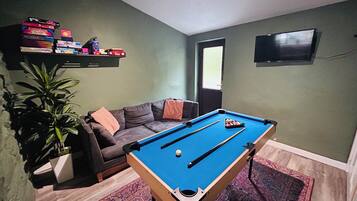 Una habitación con mesa de billar, sofá, televisor y planta.