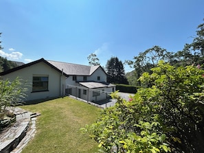 A two-story house with a sloped roof, a fenced yard, and a river in the background. - Stiniog Lodge (Blaenau Ffestiniog)