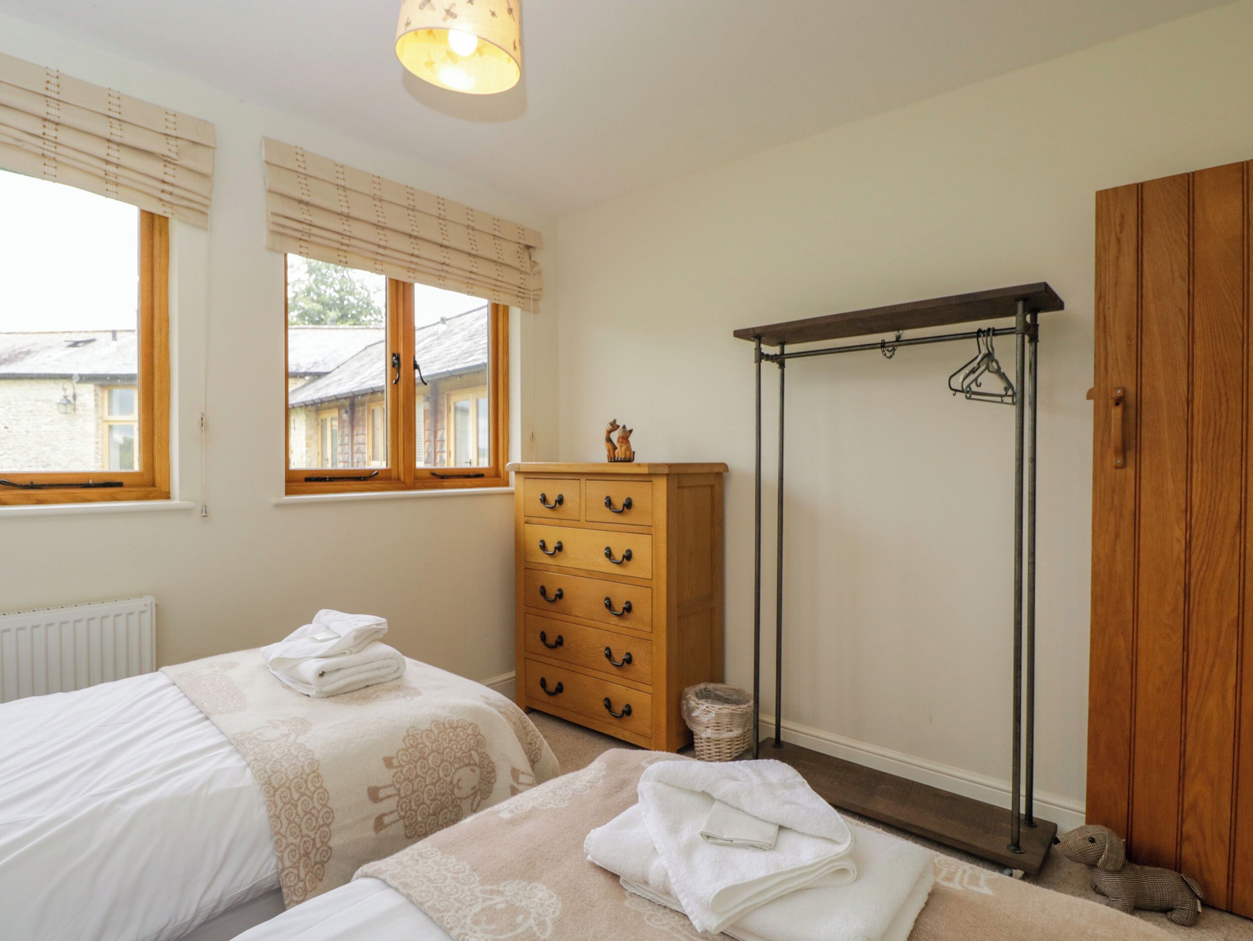 Une chambre avec deux lits, une commode en bois, un portant à vêtements et un radiateur.