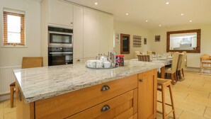 Una cocina con encimera de mármol, armarios de madera y horno empotrado. Hay un comedor con una mesa dispuesta para cuatro personas y una silla.