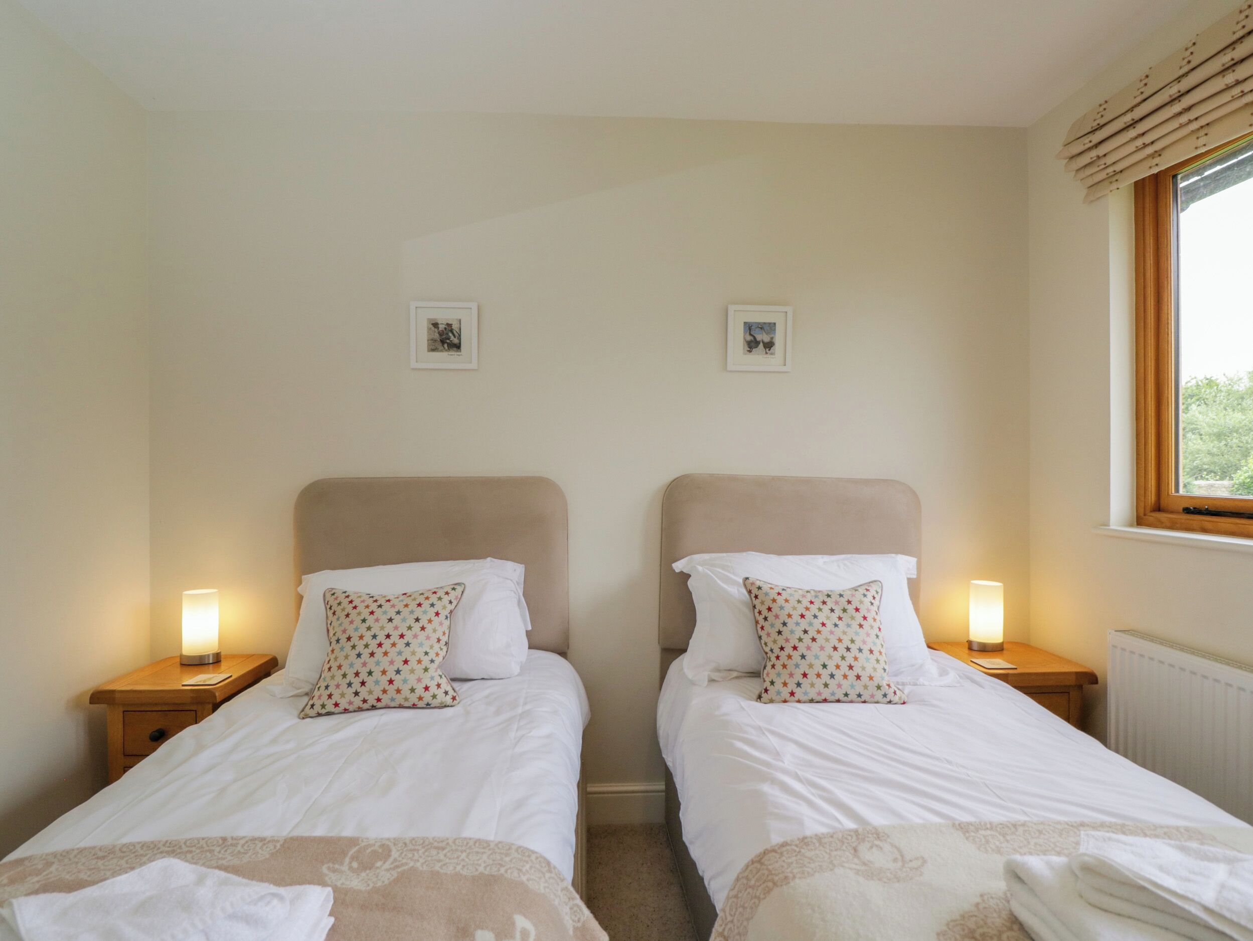A twin room with two beds, each with a nightstand, a lamp, and a window with blinds.