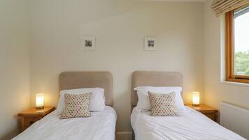 A twin room with two beds, each with a nightstand, a lamp, and a window with blinds.