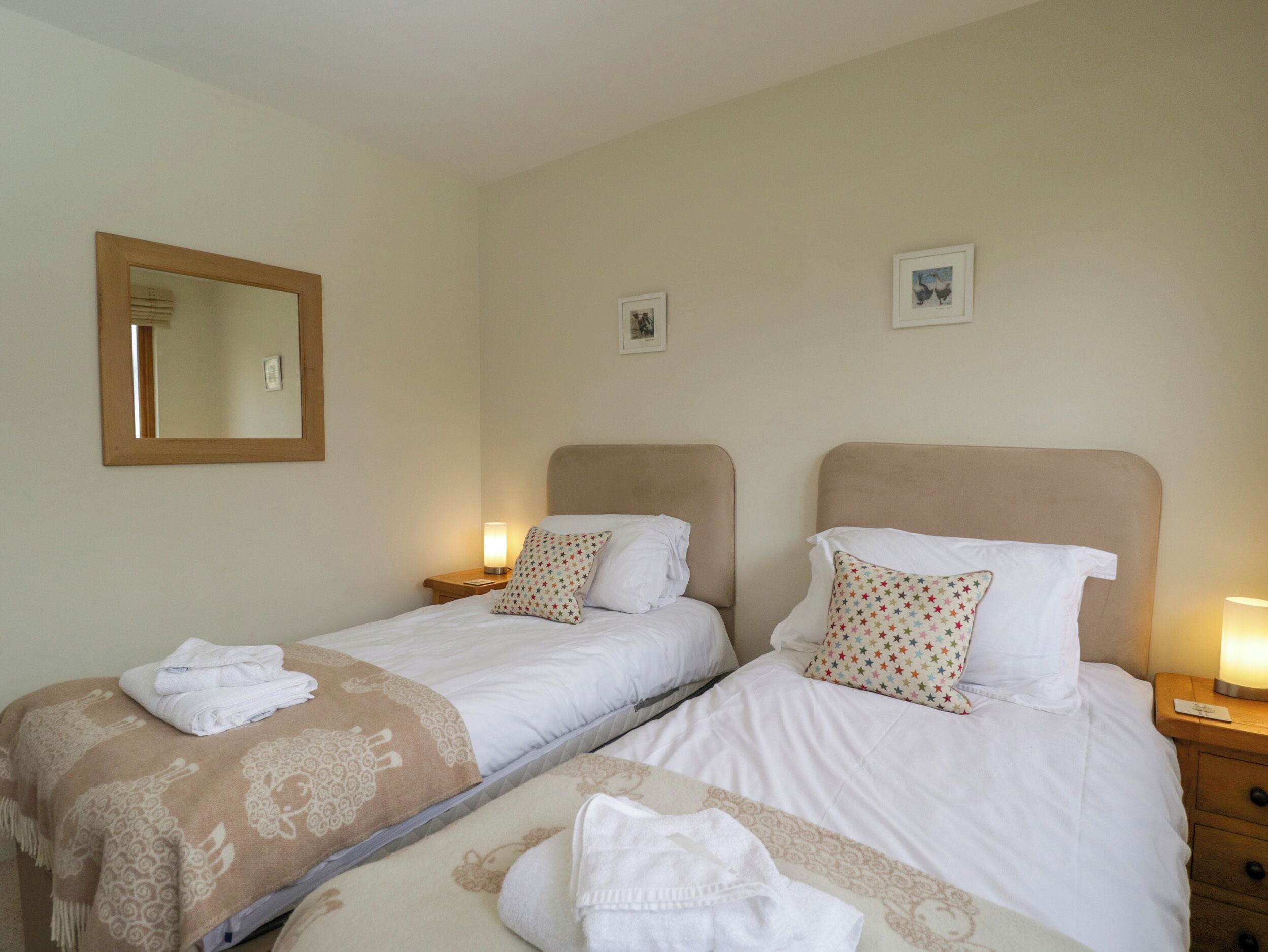 Habitación de hotel con dos camas, cada una con cabecero, mesitas de noche con lámparas y un espejo en la pared.